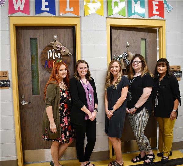 Five teachers standing outside classroom doors