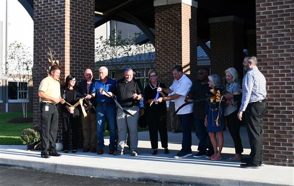 12 people hold ribbon between two brick pillars