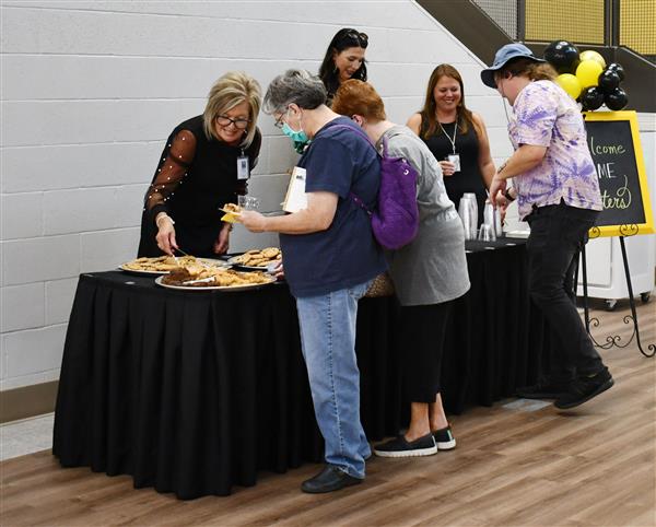 3 people behind refreshment table as others get snacks