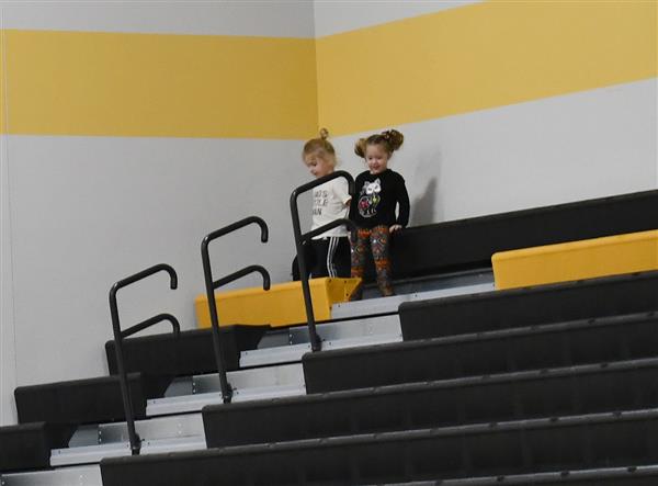 2 children sit in top corner of gym bleachers