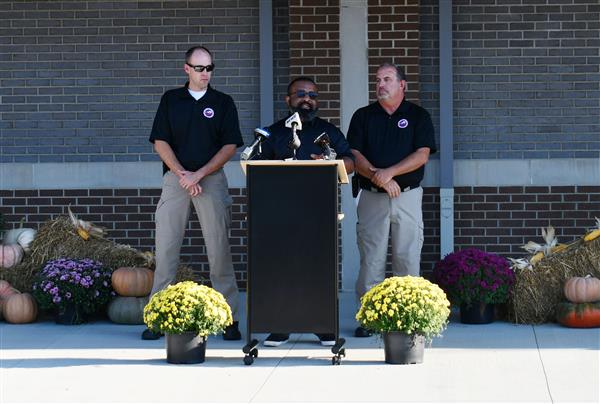 Man stands at podium with one man standing on each side.