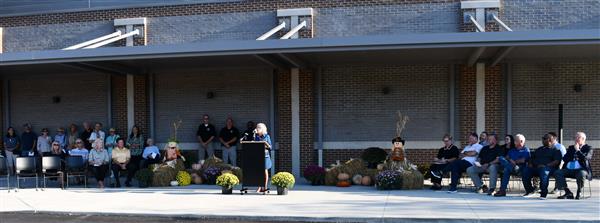 Woman talks at podium while others in seats watch, fall decor