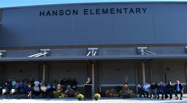 Woman at podium with people seated in tows on both sides of her in front of school