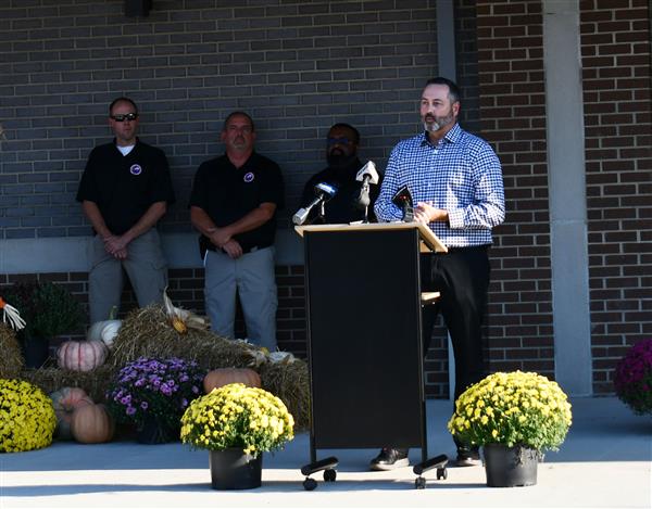 Man talks at podium with 3 men in background