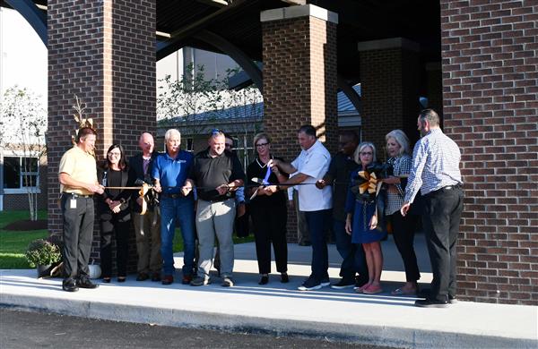 12 people in line holding ribbon between two brick pillars.