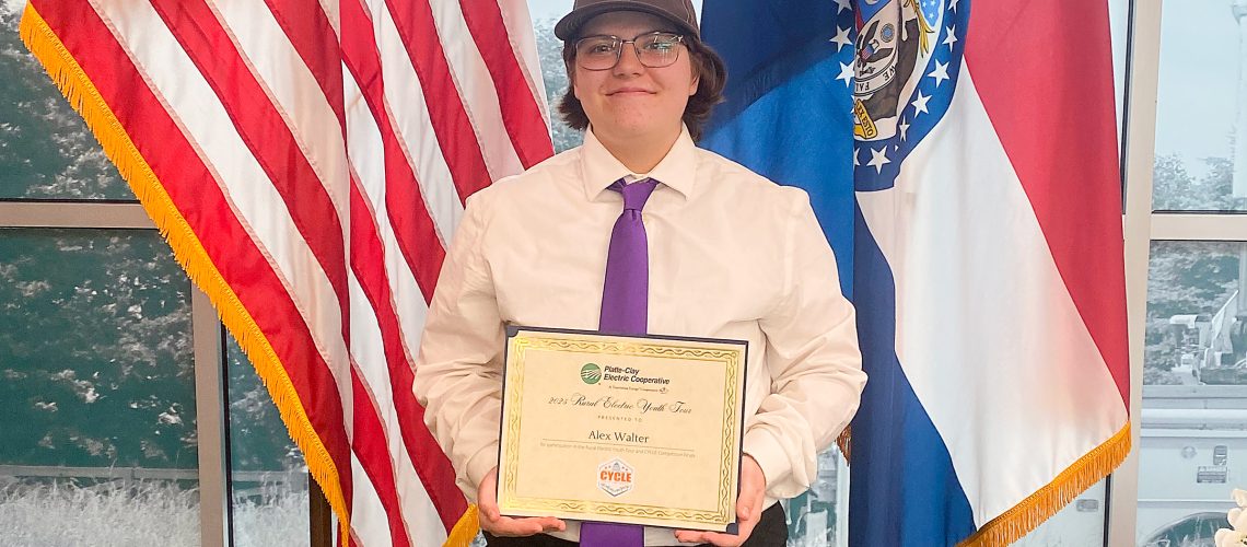 KHS junior Alex Walter poses with a certificate in front of the U.S. and Missouri flags after winning an essay contest from the Platte-Clay Electric Cooperative.