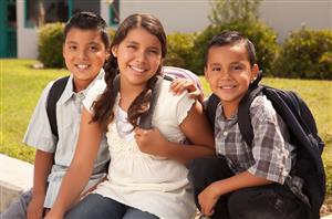 Smiling group of sibling students at different age levels sitting with backpacks outside of school