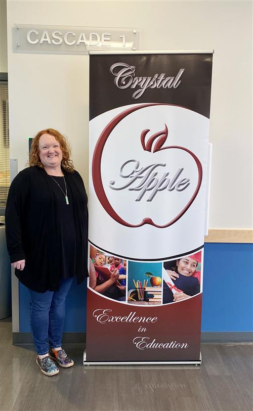 Rebecca Turner stands smiling next to the Crystal Apple award banner