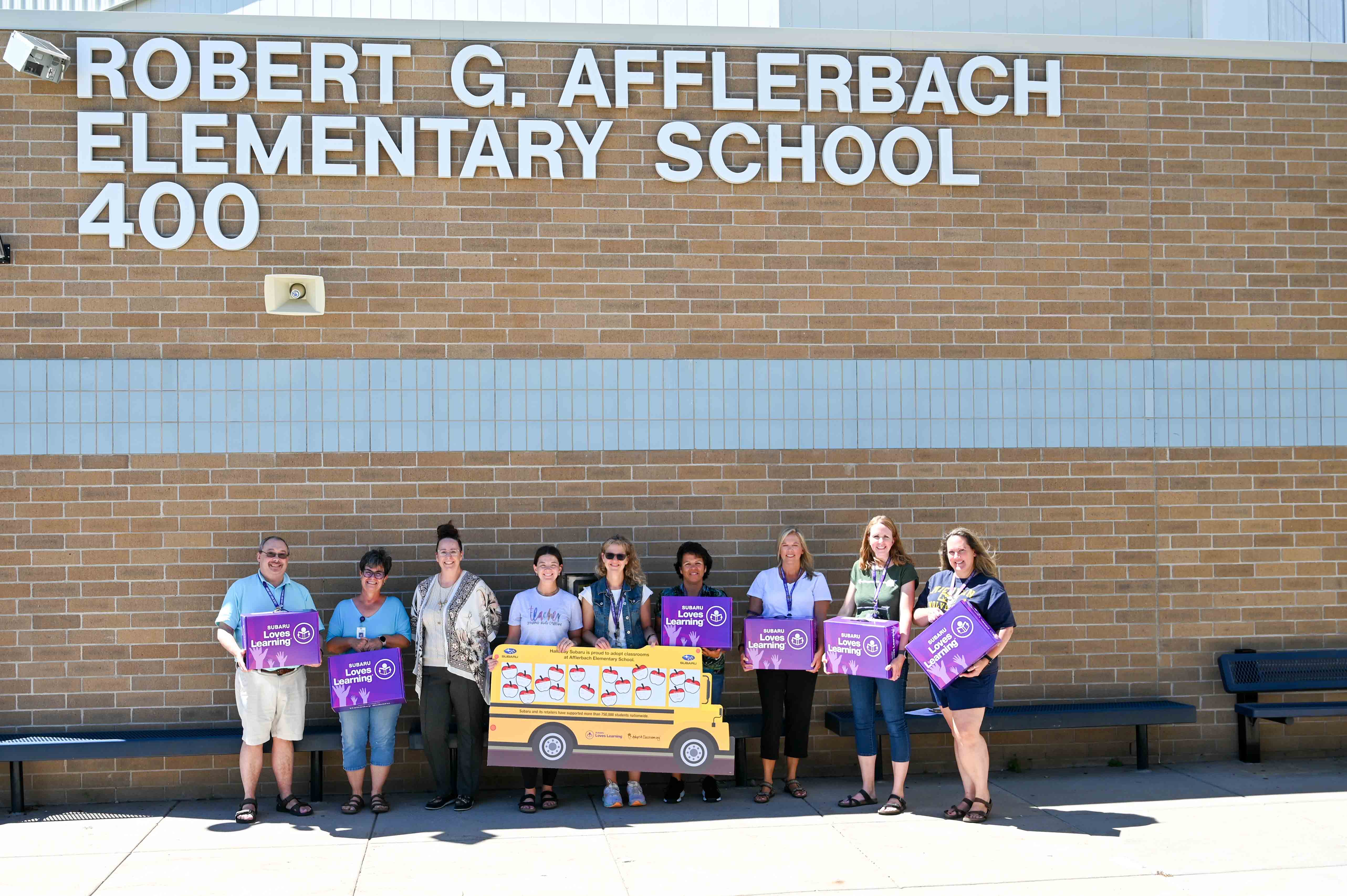 Picture of teachers under Afflerbach Sign receiving school supplies