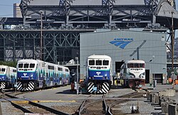 A train yard with several idle trains parked on various tracks in front of a barn with the Amtrak logo.