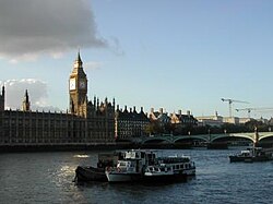 A large clock tower and other buildings line a great river.