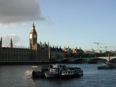 A large clock tower and other buildings line a great river.