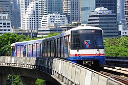 An elevated train, painted in blue, white and a red stripe and with advertisements