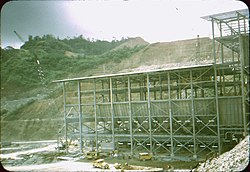Large metal building in front of a mountain with large portions cut out