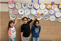 3 young students standing under the wall of paper plates that are decorated thumbnail265790