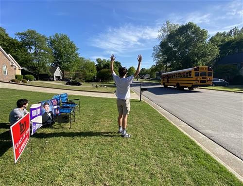 Student raising arms in victory as bus passes by his house 