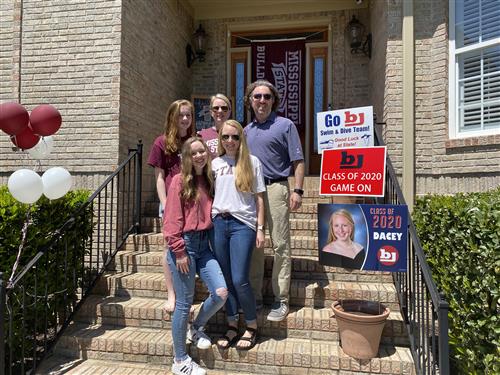 Family surrounding student on front doorstep with Mississippi State banner on door behind them 