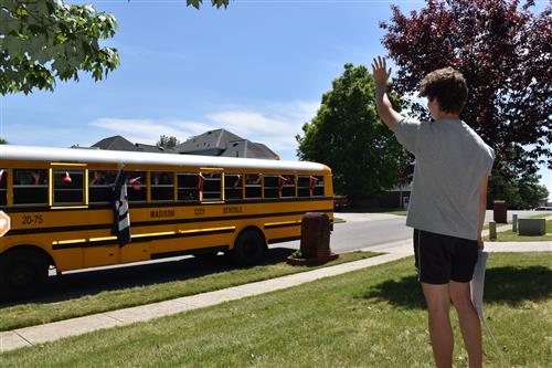 Student waving at schoolbus from front yard 