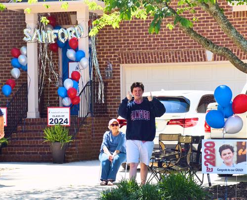 Student giving thumbs up with Sanford University Sign in background on his front door 