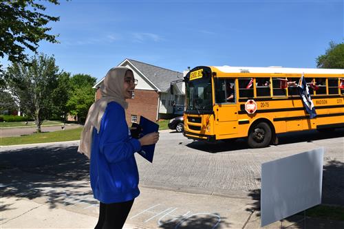 Girl waving at schoolbus from front yard 