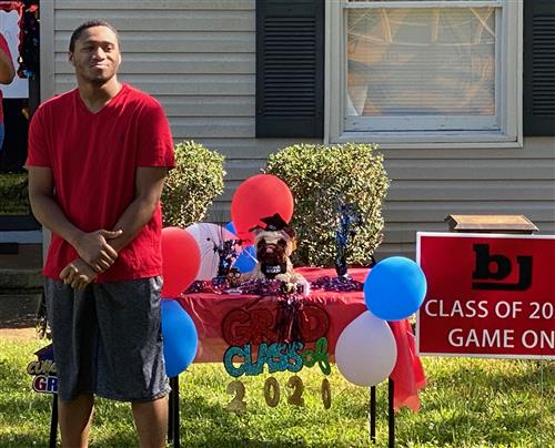 Student in front yard with balloons and Class of 2020 sign behind him 