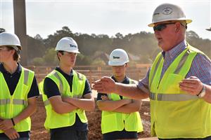 Costruction manager explaining stadium design to students in hard hats 