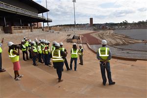 Students in unfinished bleachers overlooking infield in hardhats 