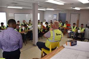 Students at table inside construction trailer getting a briefing from Turner Universal contractors 