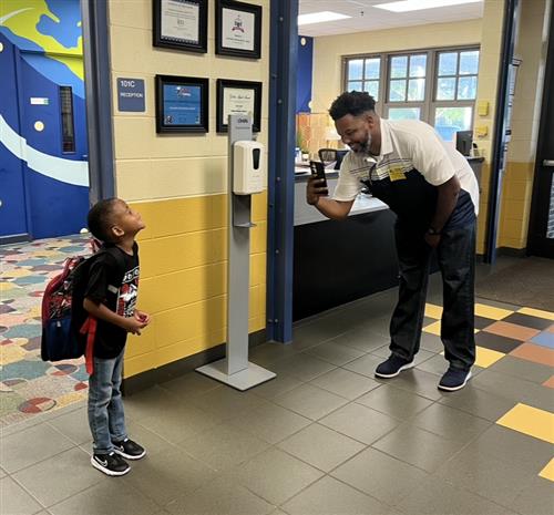 Dad taking cell pic of young smiling son wearing backpack
