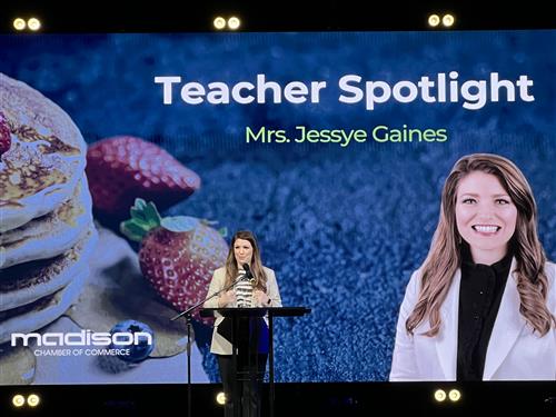 Jessye Gaines on stage with screen behind her with the heading "Teacher Spotlight"