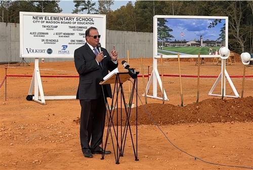 Superintendent Dr. Ed Nichols at podium with rendering behind him of the school