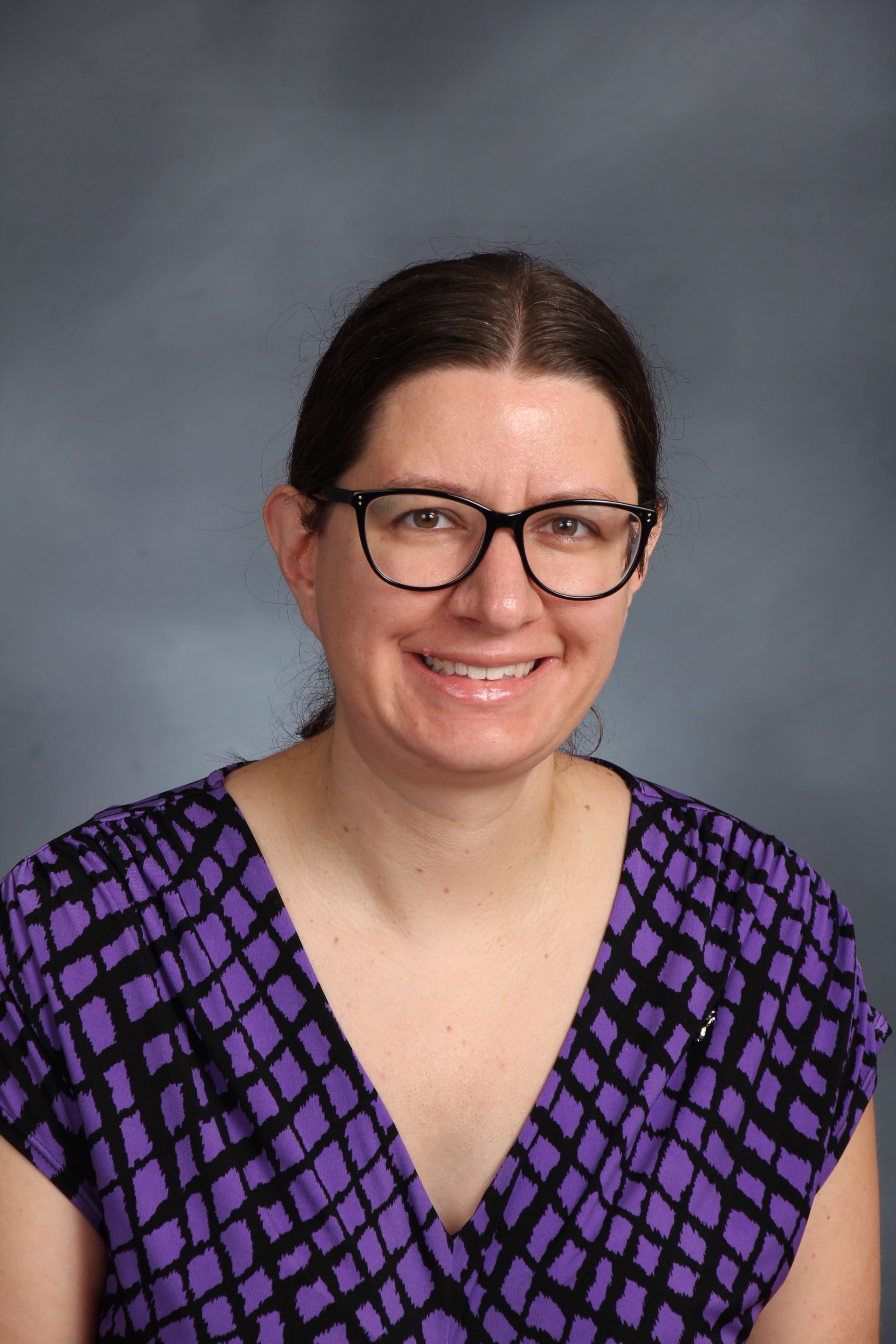 A headshot of a person wearing glasses and a purple shirt.