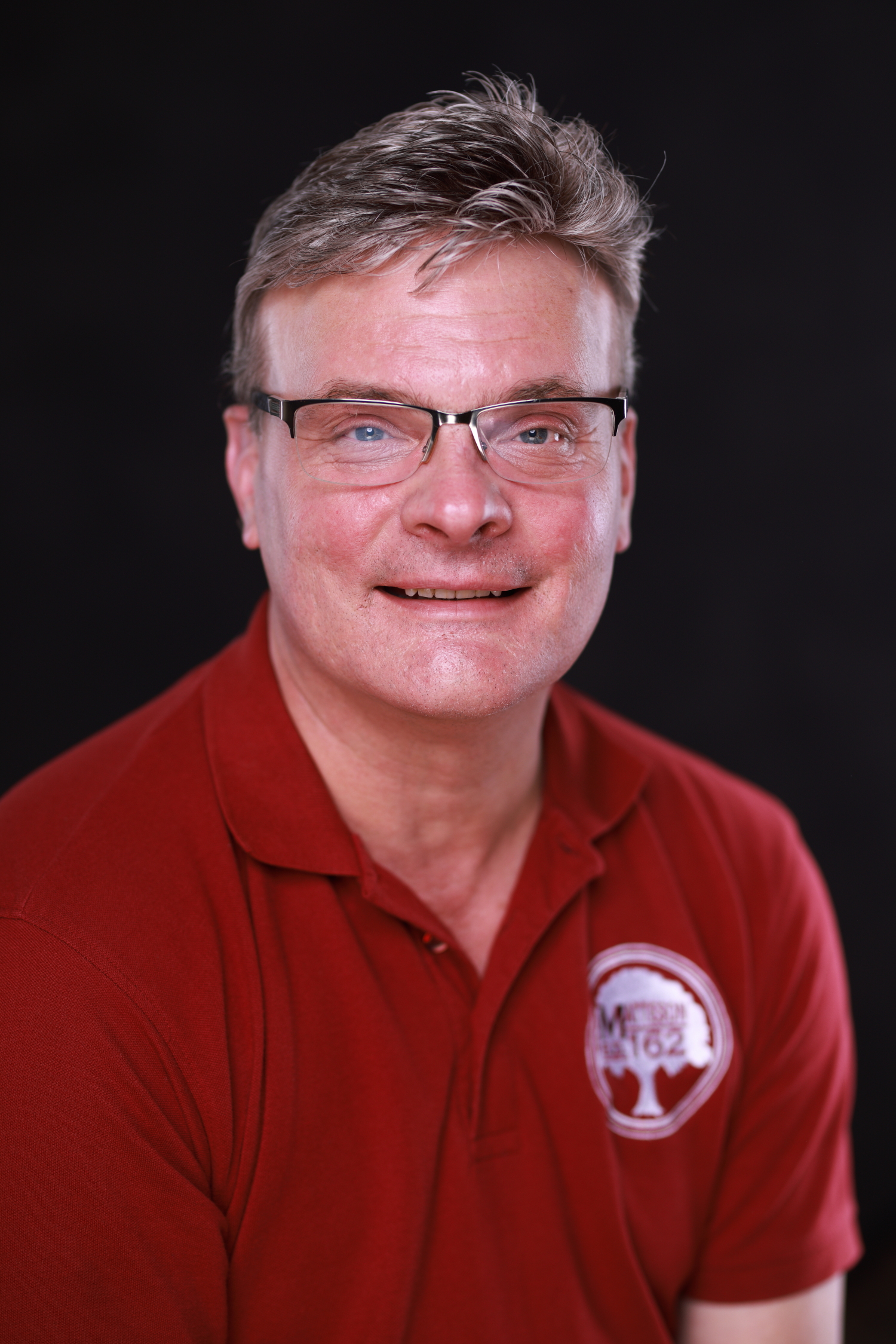 A man wearing glasses and a red shirt with a logo on it.