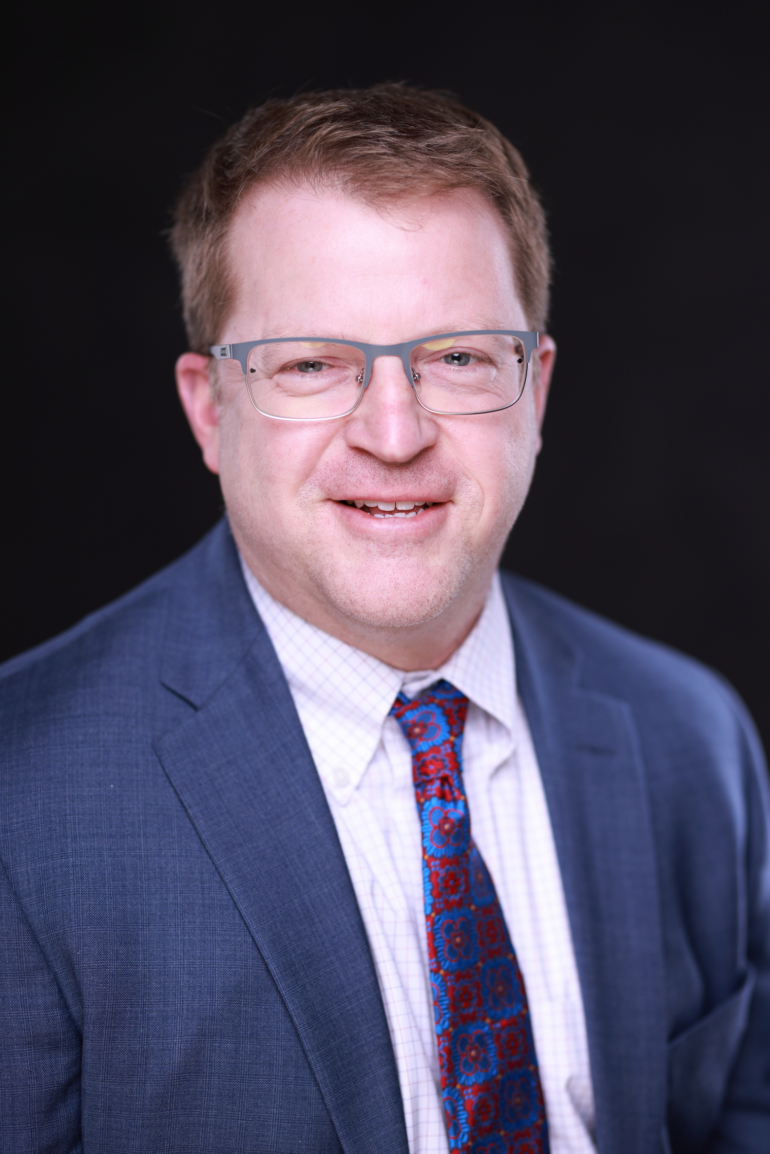 A man wearing glasses and a suit is smiling.