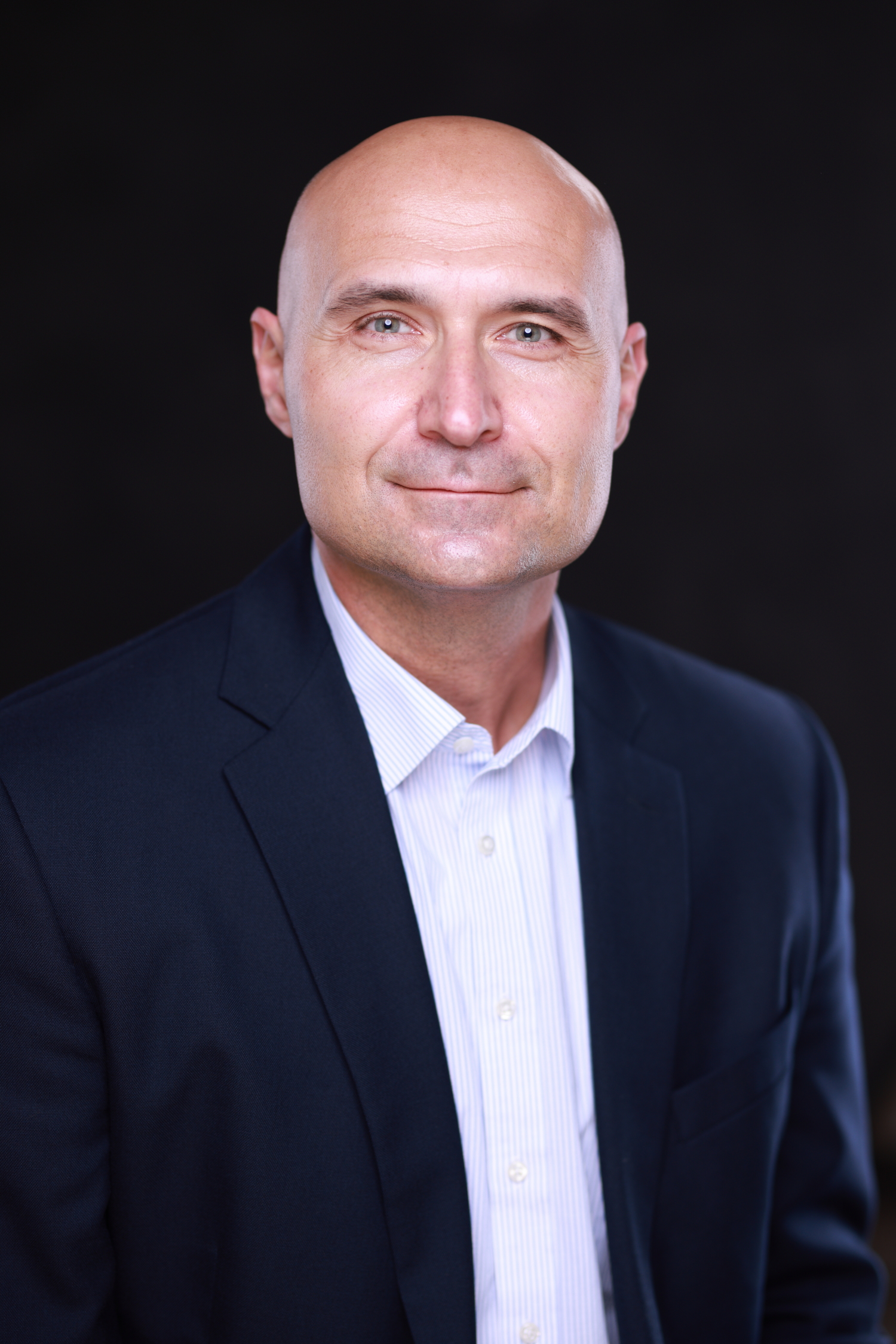 A headshot of a bald person in a suit.