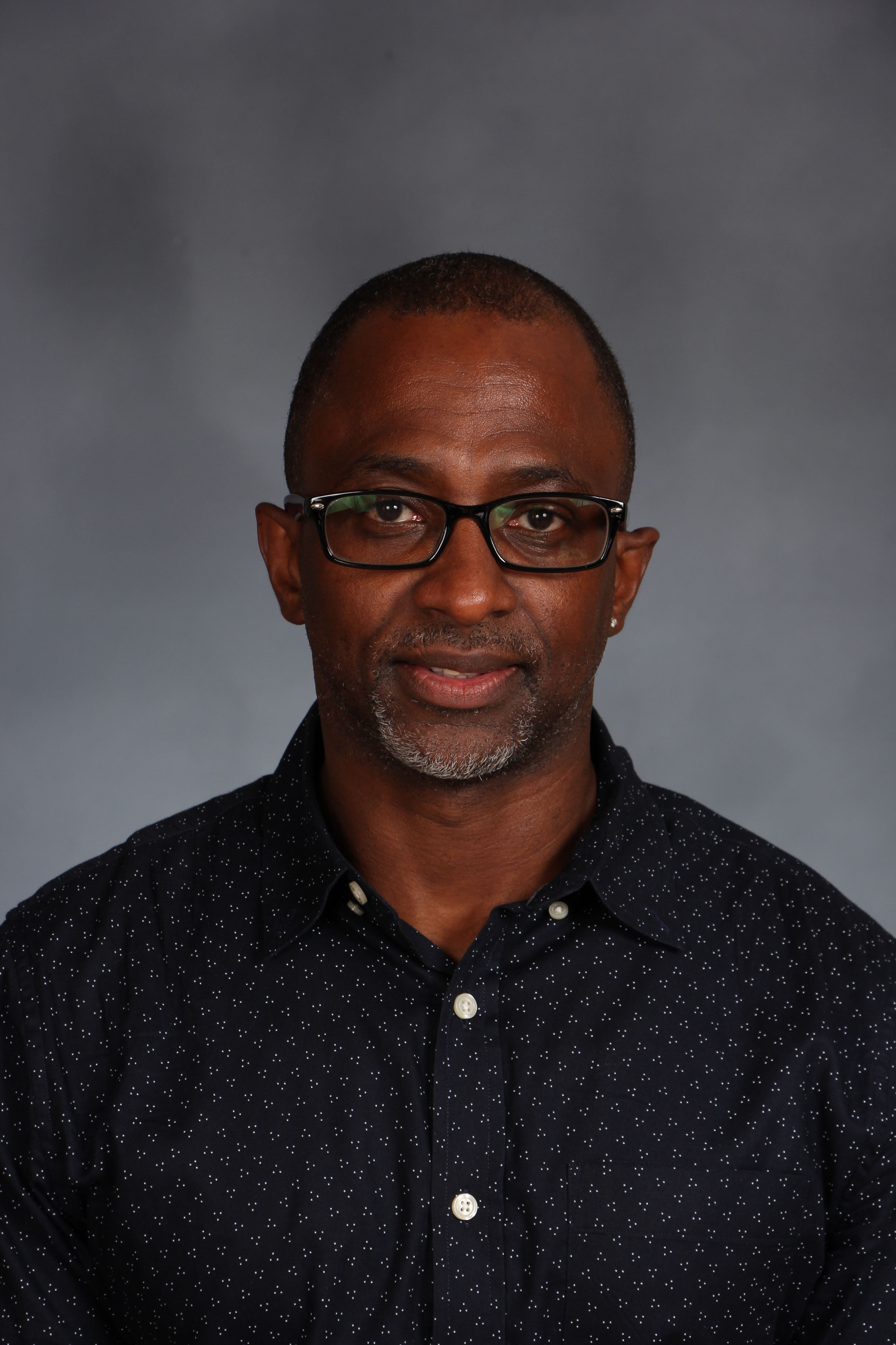 A headshot of a person wearing glasses and a black shirt with black dots.