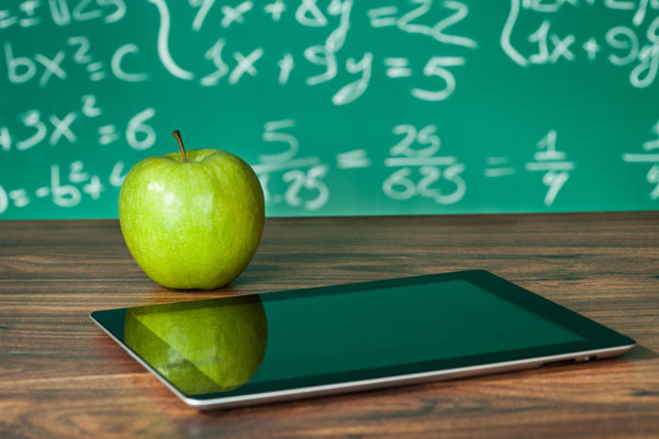 Stock photo of a tablet device and green apple on a teacher's desk