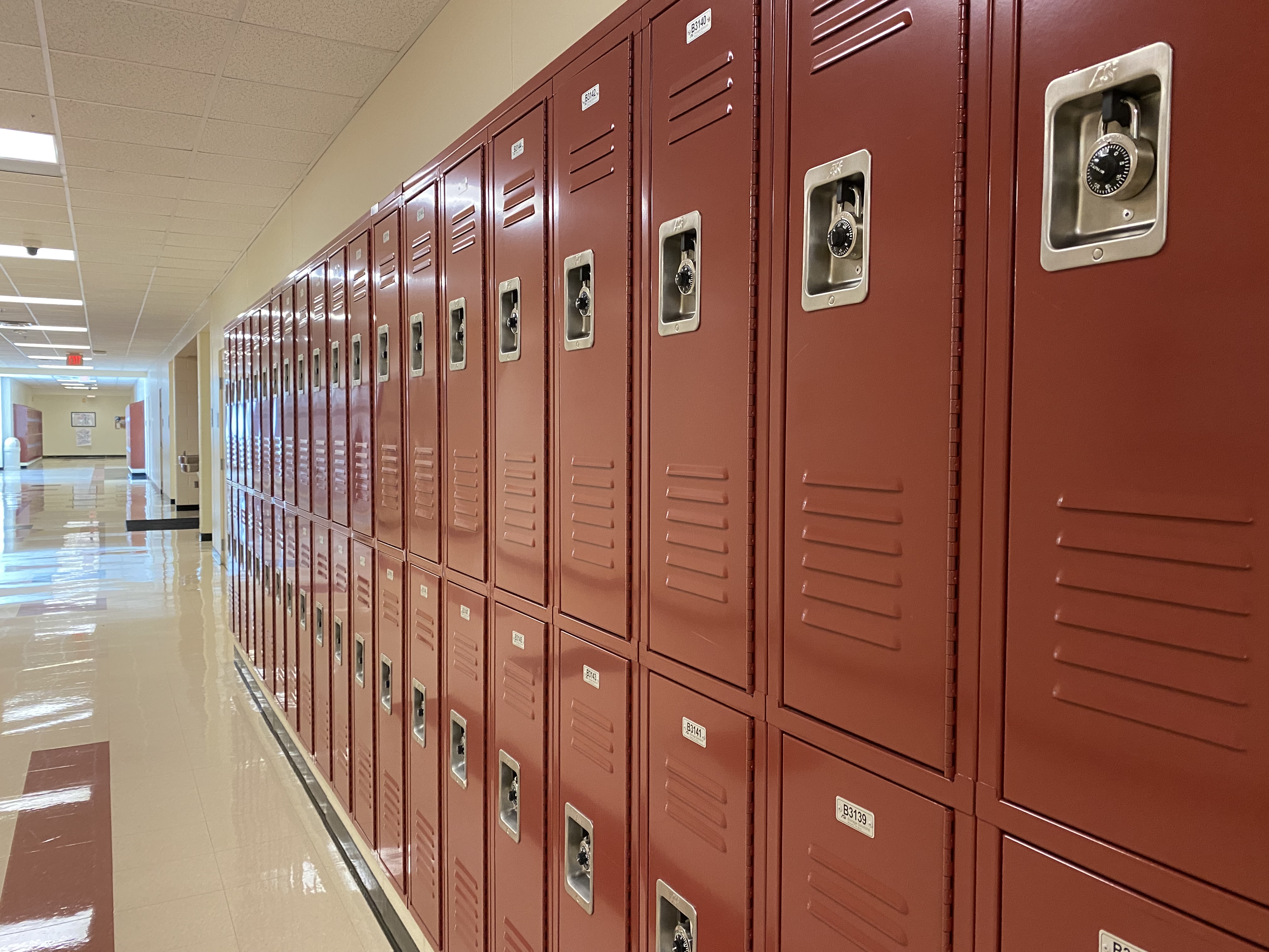 An empty school hallway with dozens of red lockers.