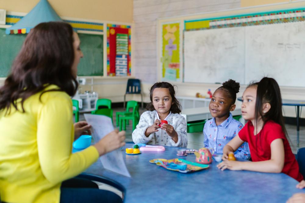 A teacher is sitting at a table with three students.