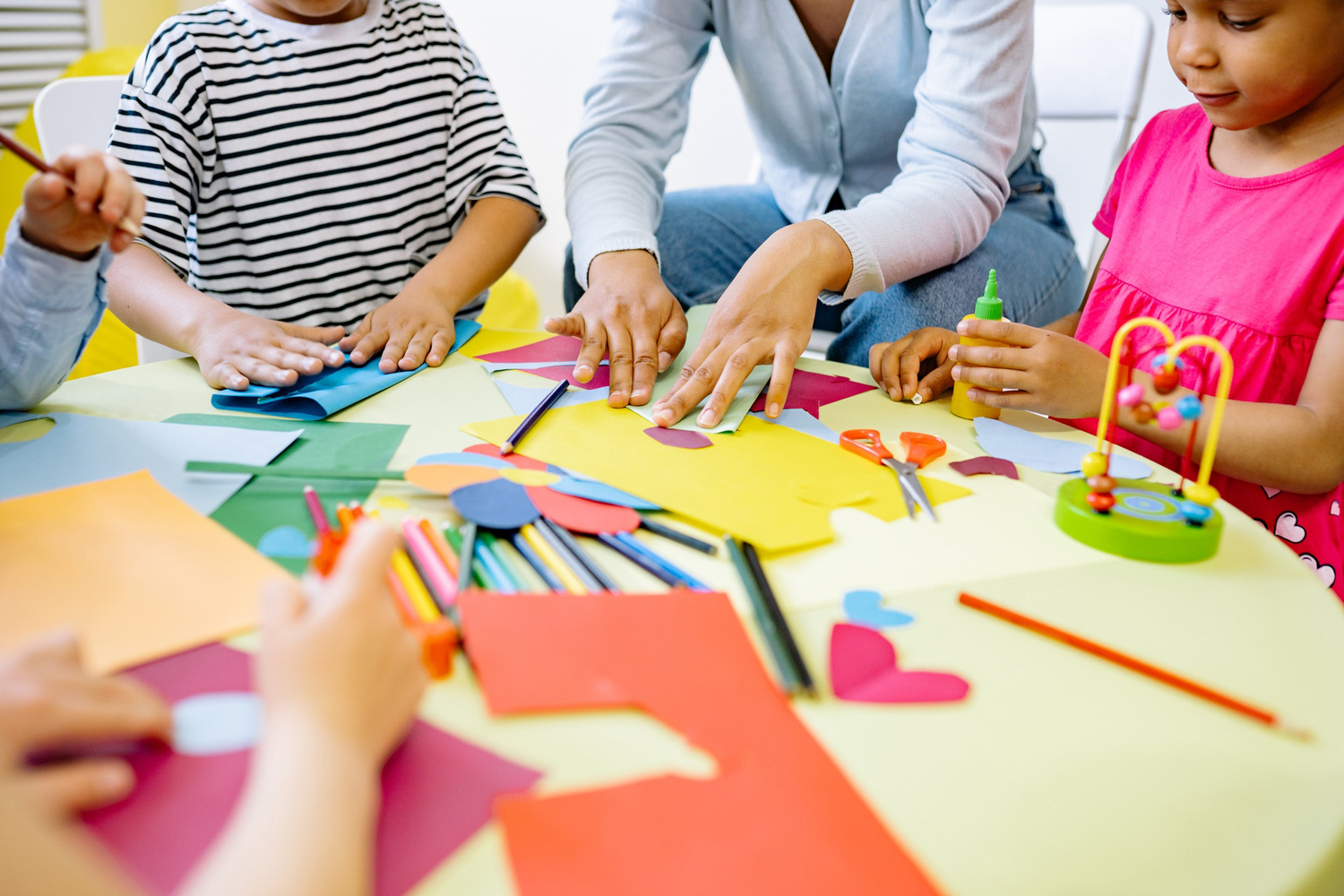 A group of children are sitting around a table with a teacher, working on an art project.