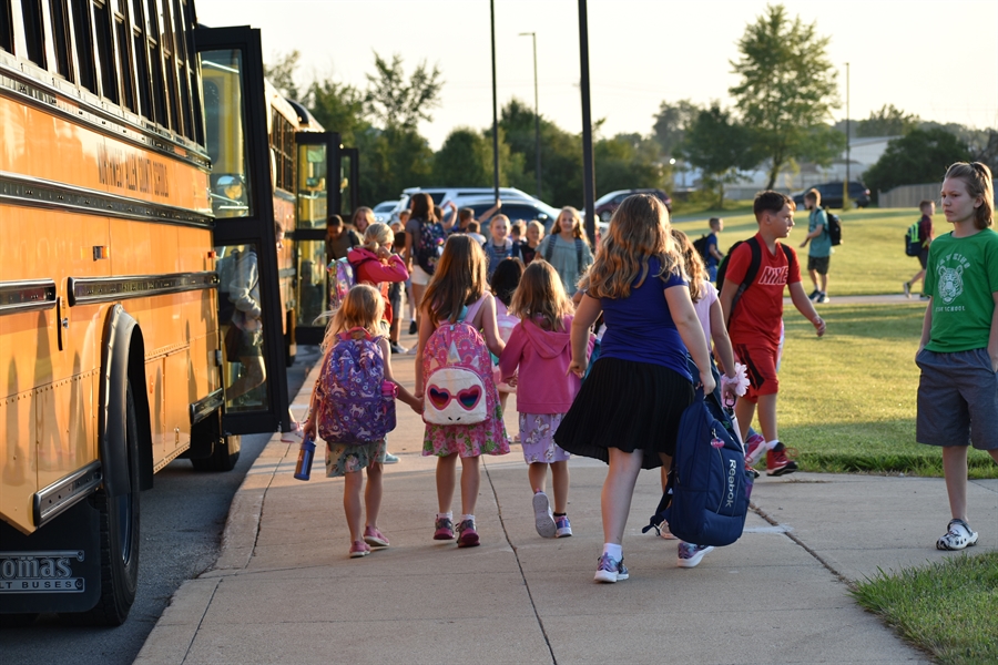 children holding hands walking from the bus