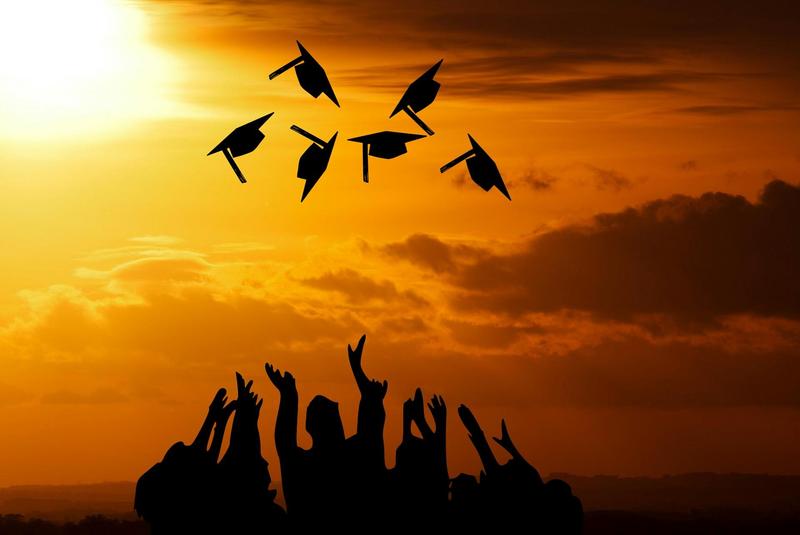 Silhouette of graduates tossing caps with a sunset in the background