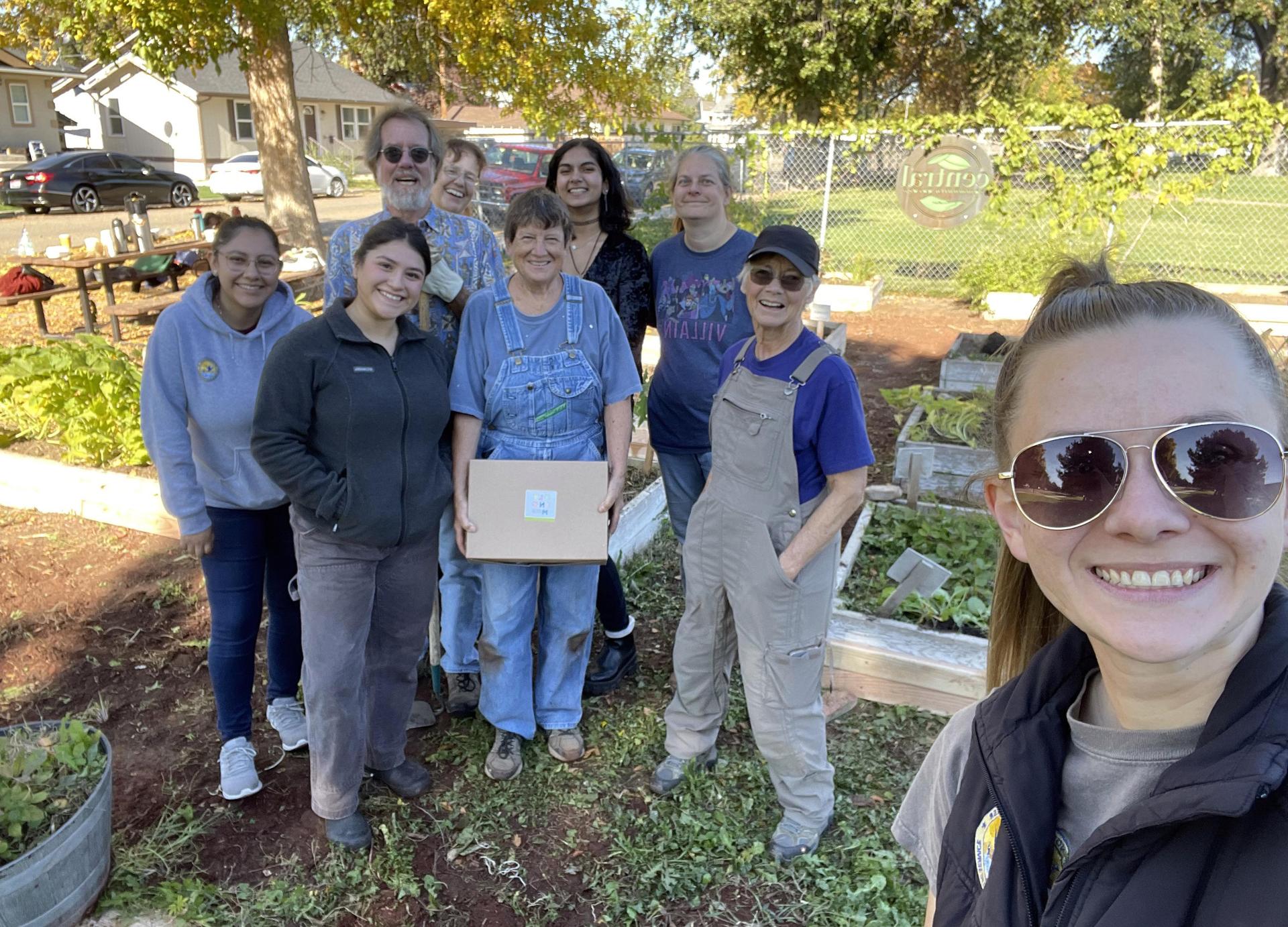 Woman in sunglasses takes a selfie with eight volunteers dressed for gardening.