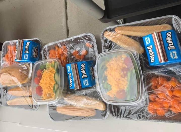 School lunches wrapped in plastic await pickup outside a school.