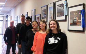 Photography students line up in the hallway next to their framed photos, along with teacher Terrell Moffett.