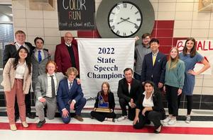 Team members and coaches pose in front of the 2022 state speech champion banner.