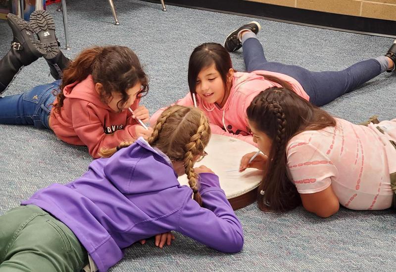 Four elementary-aged girls lay on the floor around a drum.