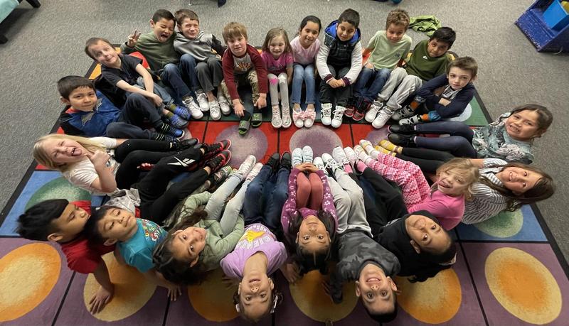 Overhead view of kids sitting on the floor in a circle, showing off their shoes.