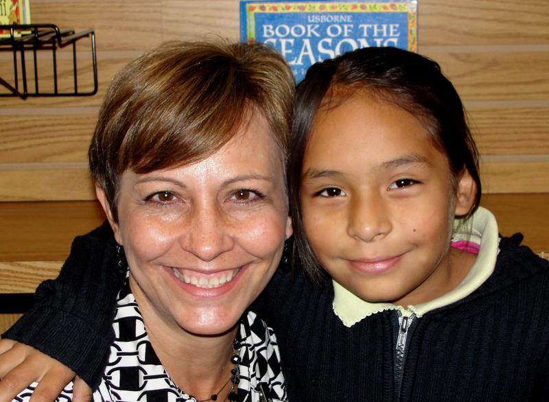 Closeup of a woman with short dark blonde hair next to a girl with long dark hair, both smiling.