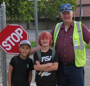 Male crossing guard poses with two young boys outside the school.